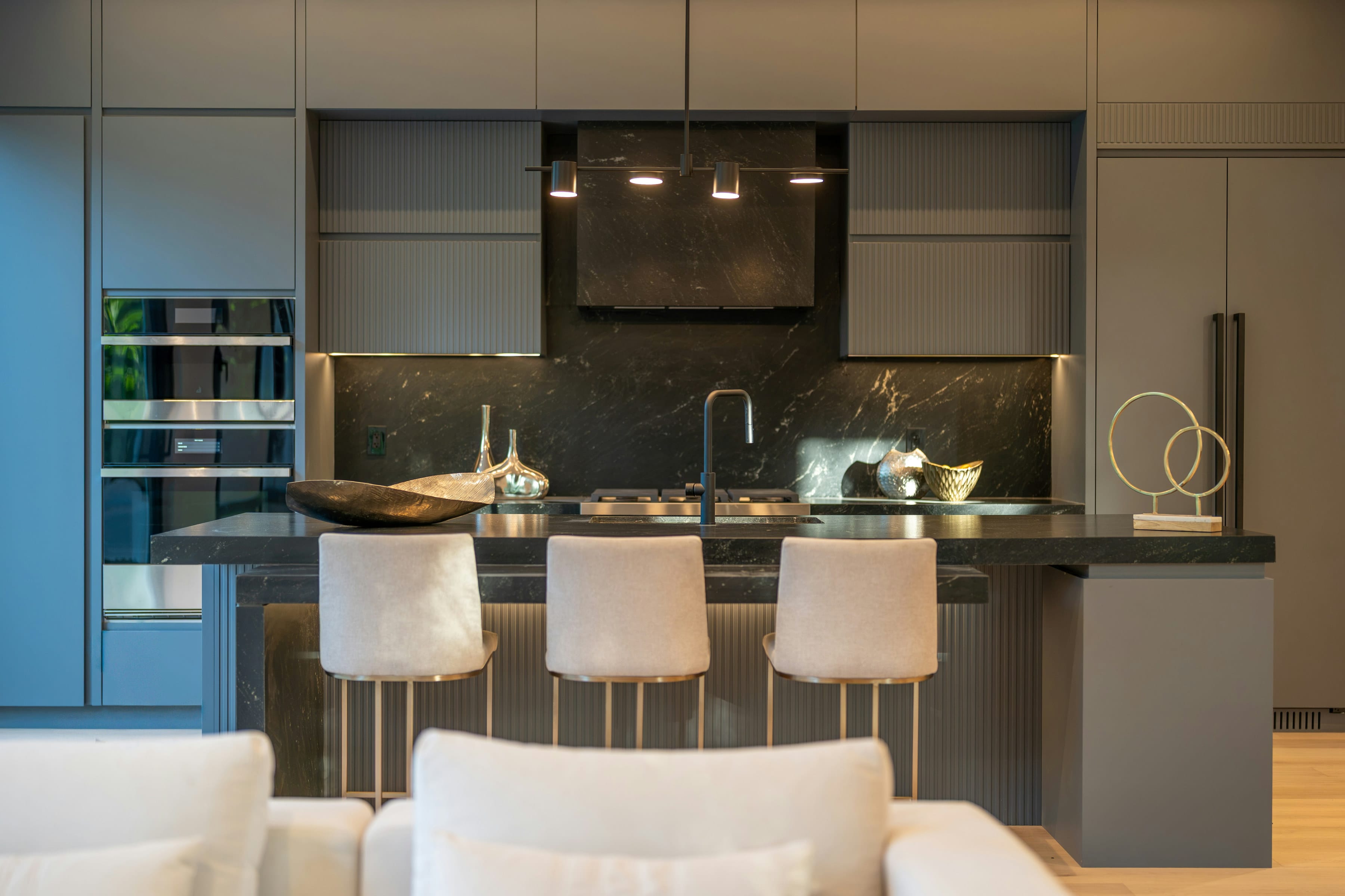 Dark grey island with marble splashback, pendant lights and cream stools