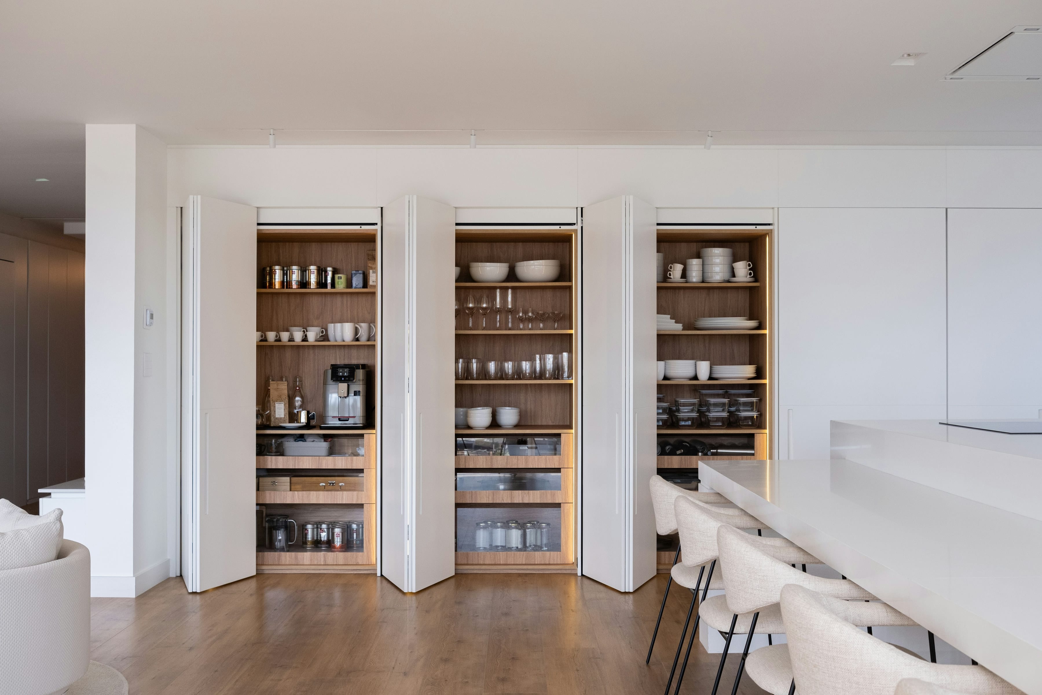 Folding pantry doors open to oak shelving in a modern kitchen