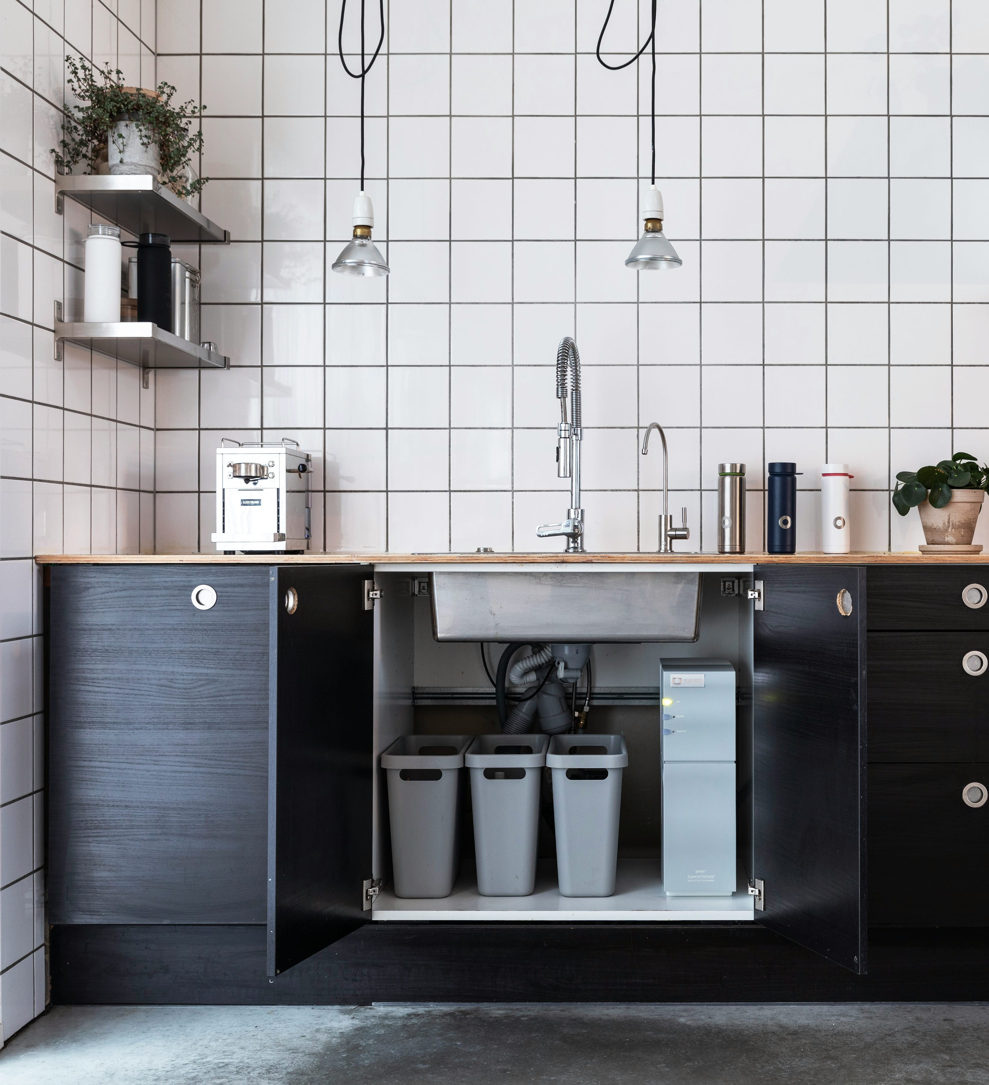 Black under-sink cabinet opened to show three sorted waste bins and tidy pipework