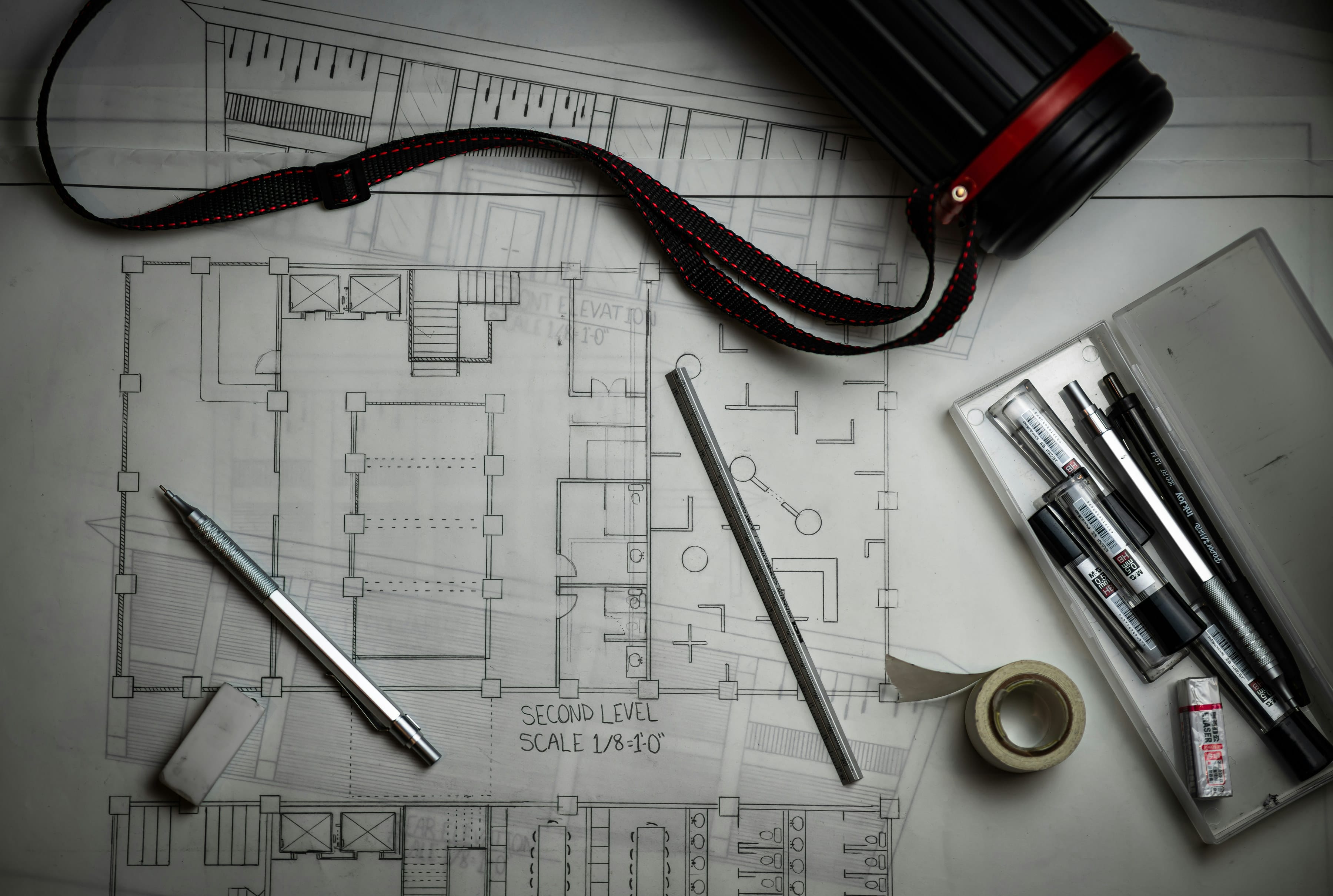 Architectural floor plan with pens, tape and camera strap, flat lay