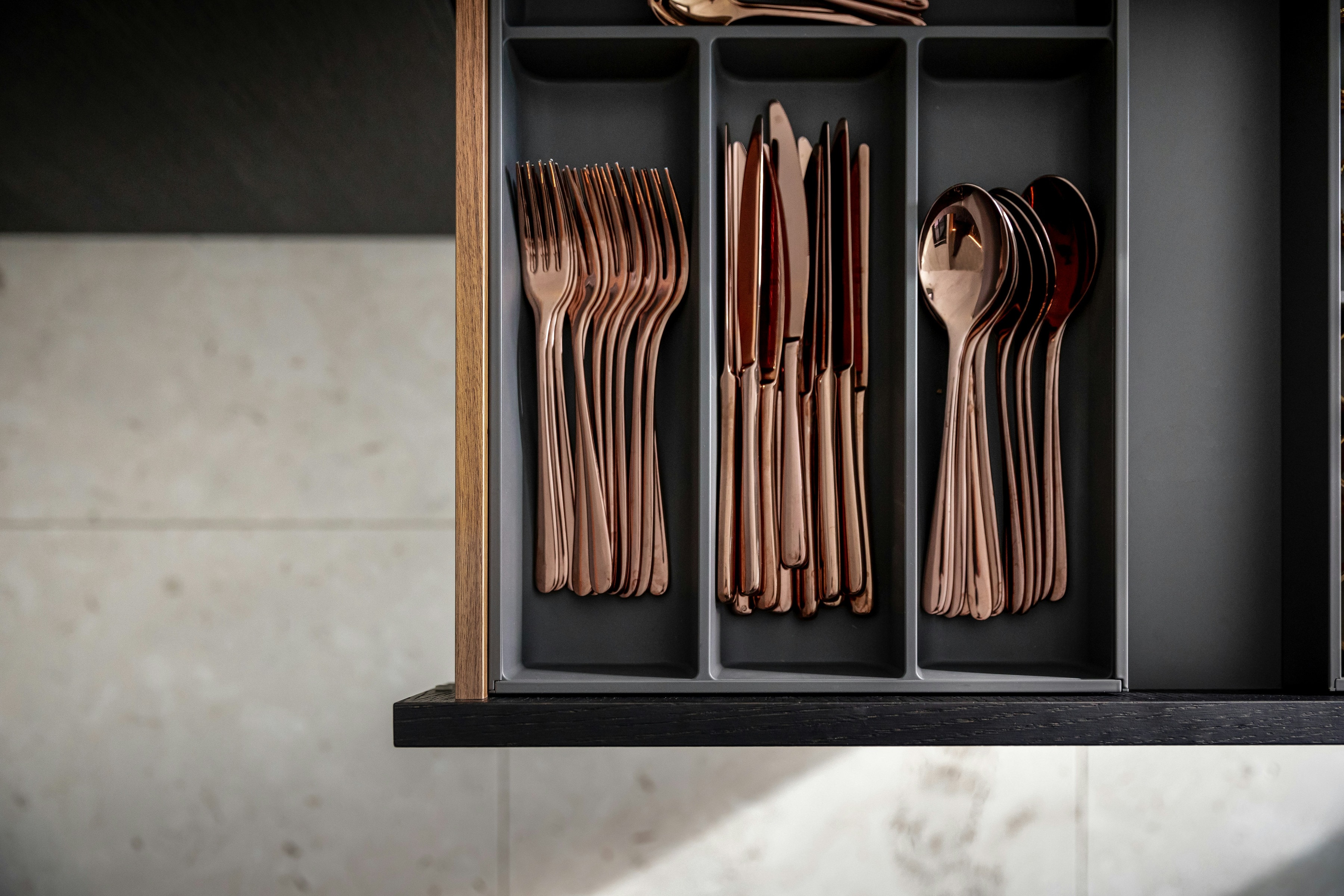 Black drawer insert with upright copper cutlery against terrazzo worktop