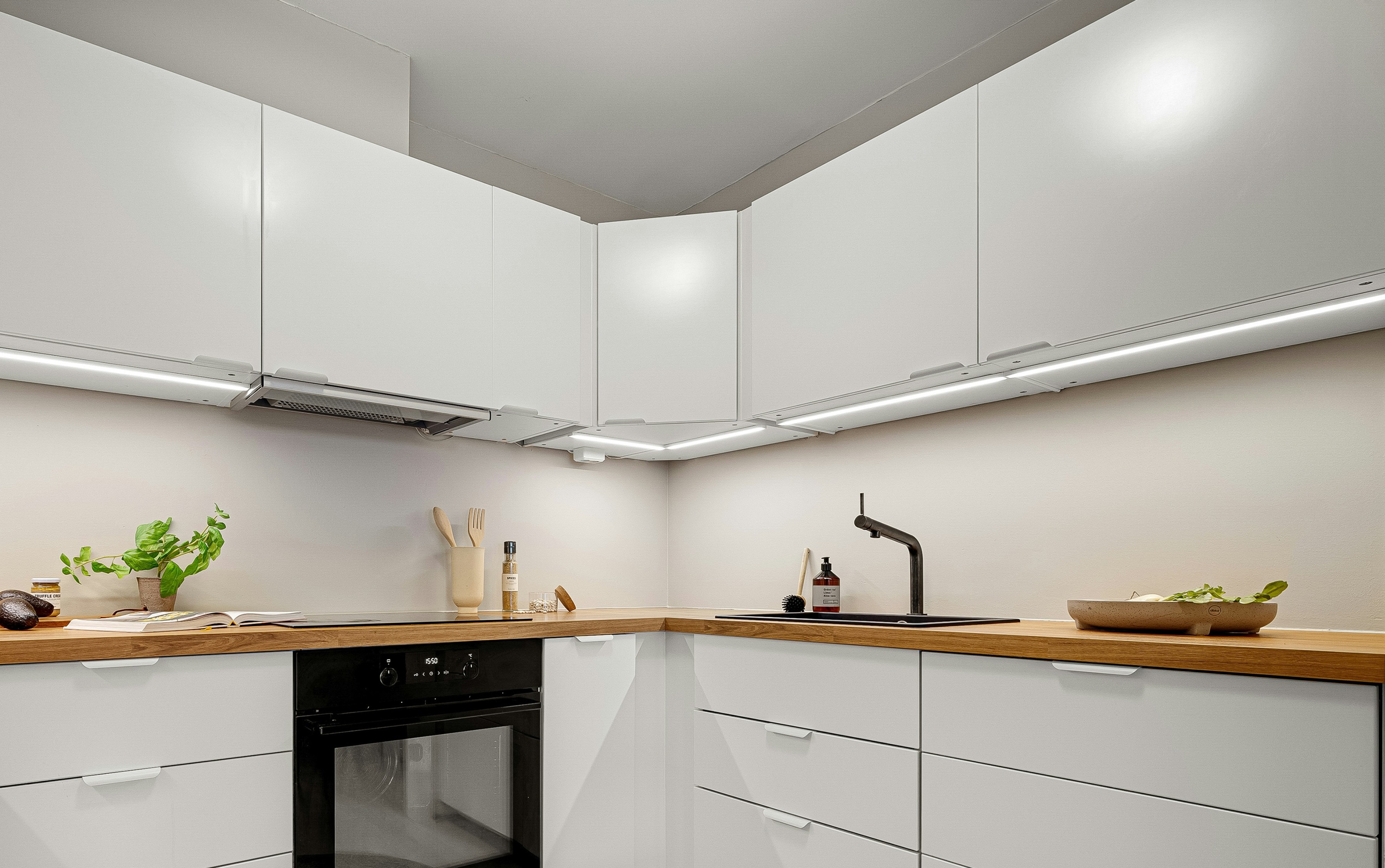 White L shaped kitchen with oak worktop, angled corner wall cabinet and warm LED strips