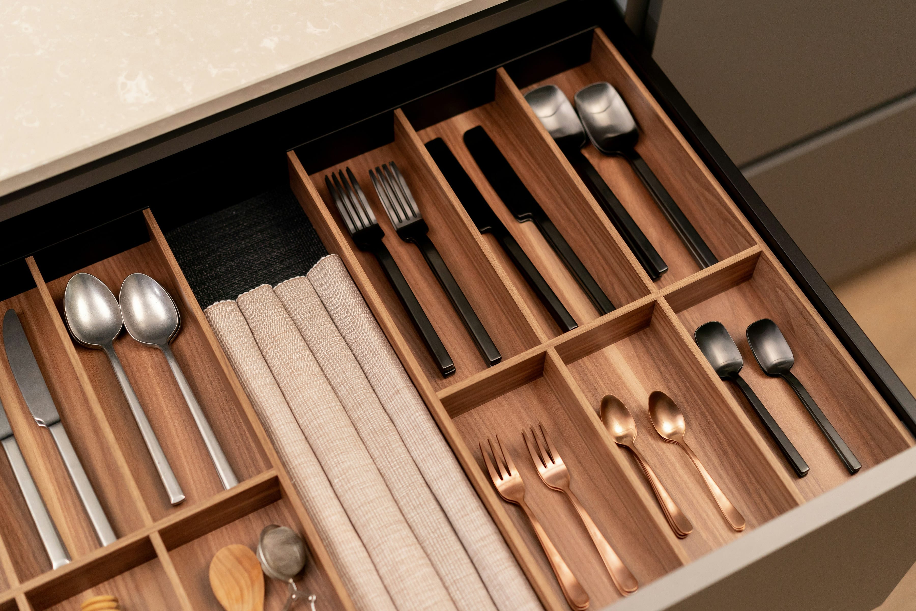 Walnut drawer cutlery tray holding copper cutlery in a dark kitchen