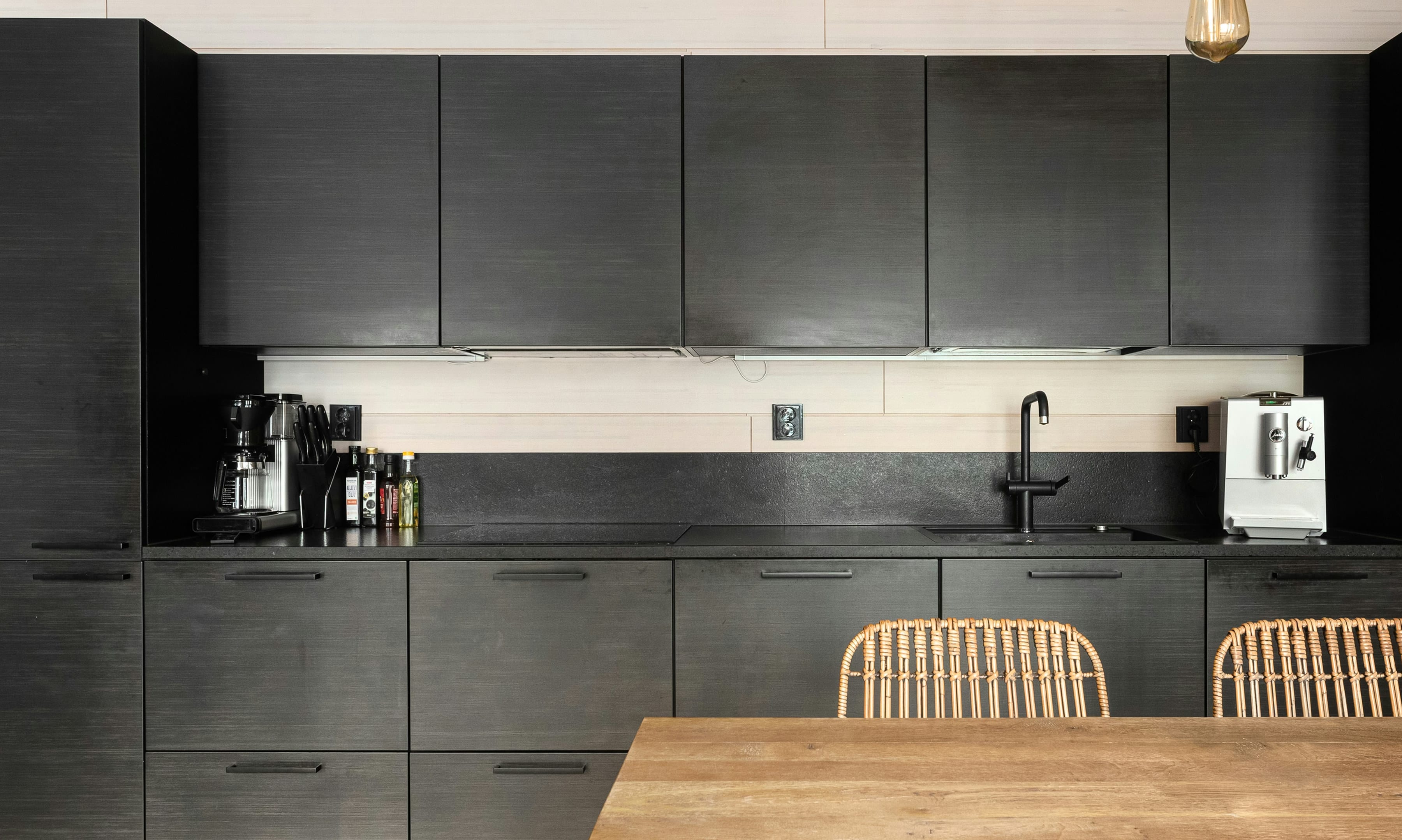 Matte black oak veneer kitchen with black tap, warm pendant bulbs and an oak table in front
