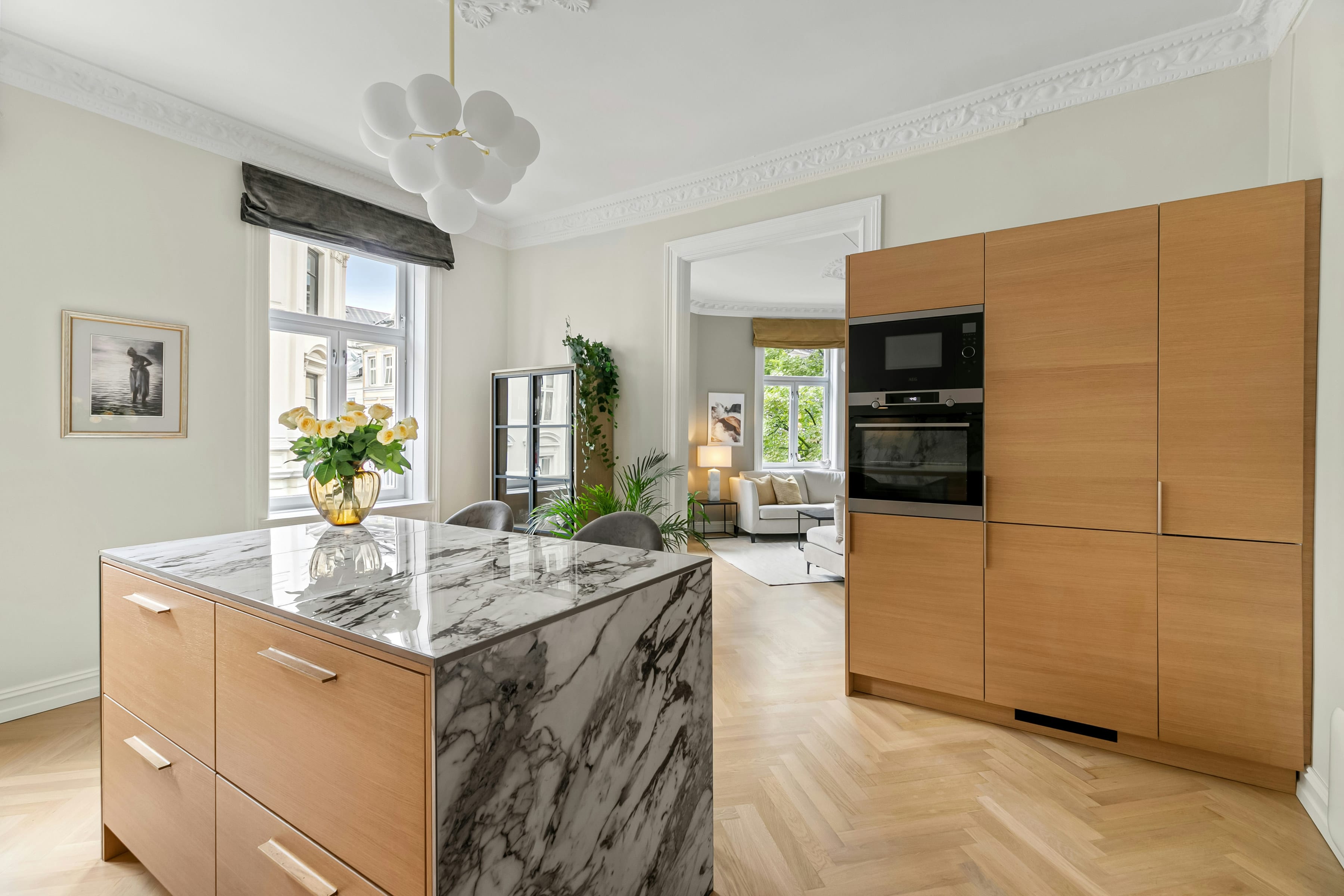 Marble waterfall island beside a tall oak cabinet wall with built in oven in a bright apartment