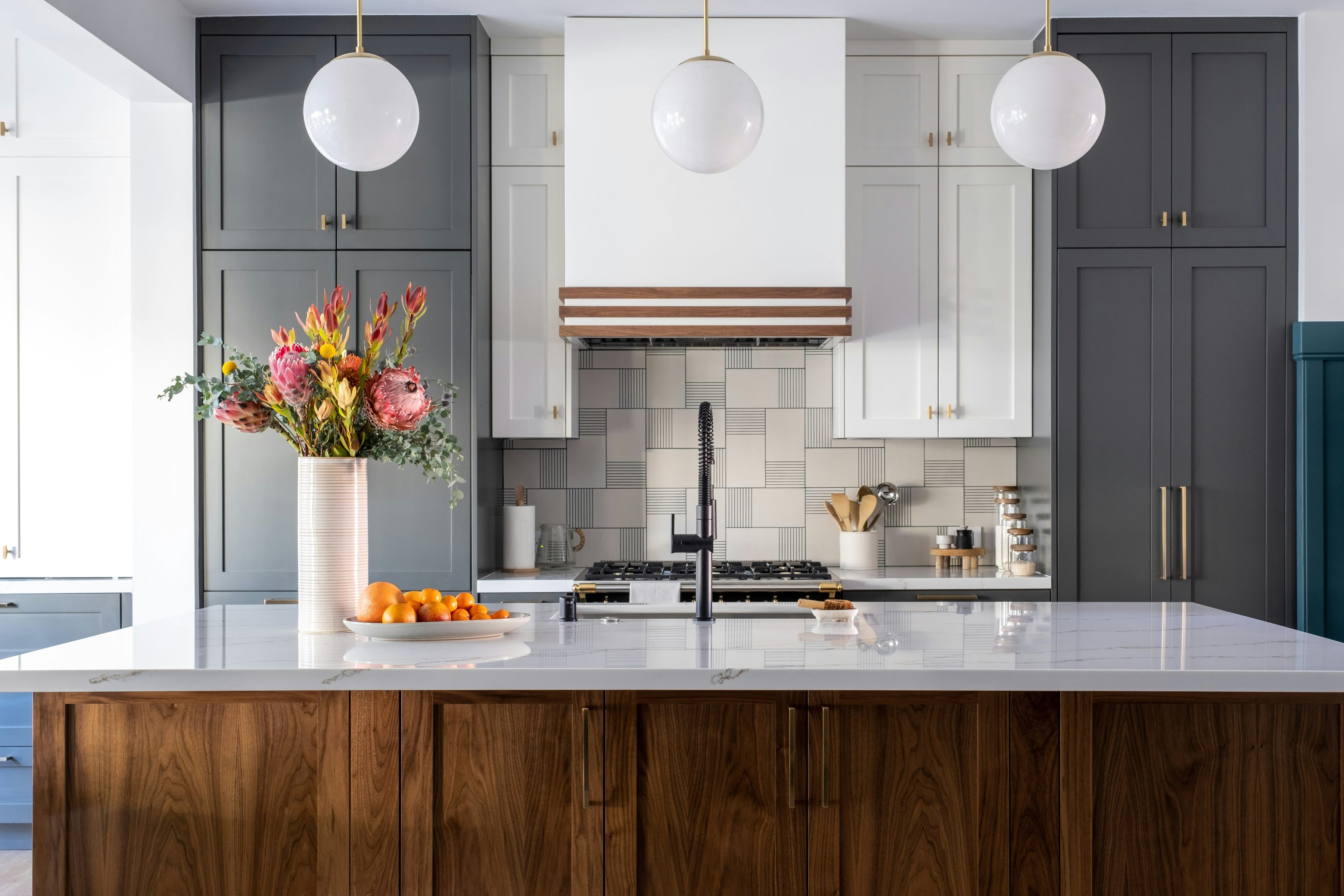 Walnut paneled island with white marble top, globe pendants, grey cabinets and brass handles