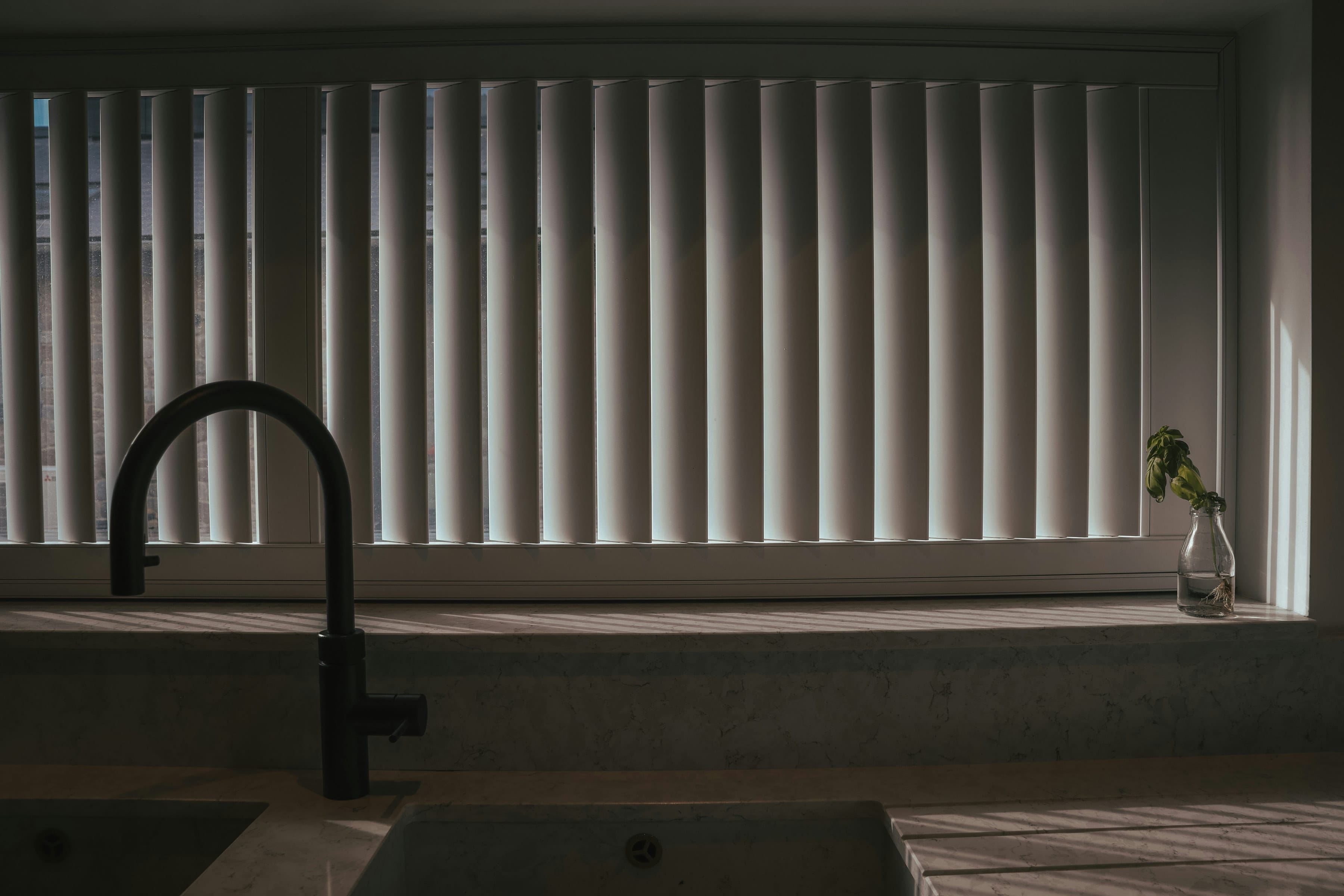 Black arched tap and marble sill in low sun through a wide louvered window